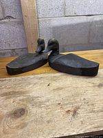Two carved wooden ducks, black painted, on a wooden surface against a gray concrete block wall.