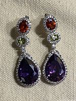 Close-up front view of the pair of purple amethyst crystal tear drop earrings with orange and light green oval stones and clear rhinestones set in silver-tone metal.