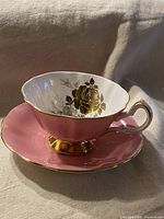 Side view of pink Queen Anne teacup with gold floral interior and gold trim on handle and foot, placed on matching pink saucer.