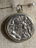 Round sterling silver locket with detailed raised relief of a woman's profile featuring flowing hair and an elaborate decorative headpiece.