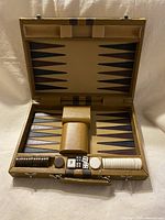 Front view of the open portable backgammon case showing the playing surface, chips, dice, and dice shakers in place.