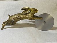 Side view showing the running brass bunny with attached circular stainless steel pizza cutter wheel, detailed features visible on the bunny.
