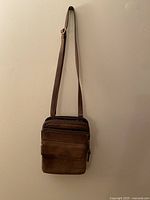 Full view of the vintage brown leather crossbody bag hanging against a wall, showing the adjustable strap and main body.