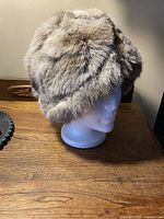 Front-right angle view of a fluffy vintage rabbit fur hat displayed on a white mannequin head, showing the texture and color of the fur.