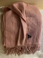 Folded dusty pink scarf with fringe edges.