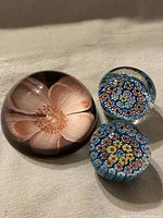 Three vintage paperweights, one large floral pink design and two smaller millefiori cane designs on blue backgrounds.