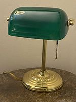 Front view showing green glass shade and polished brass base with pull chain.