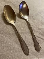 Two vintage sterling teaspoons displaying their front side and engraved handles.