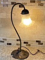 Full view of vintage brass lily pad table lamp illuminated showing frosted tulip glass shade and curved goose neck arm