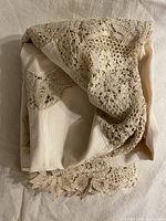 View of folded beige linen tablecloth showing crochet lace edge folded over fabric.