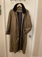 Full front view of vintage Winnie Magee long coat hanging on hanger showing brown herringbone linen fabric with black velvet collar and button closure.
