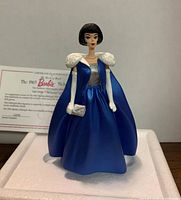 Front view of the Barbie figurine showing the blue gown, white gloves, fur stole, and silver clutch with Certificate of Authenticity in the background.