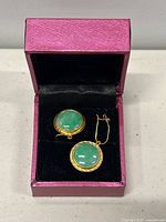Pair of gold earrings with green stone inlay in a pink presentation box.