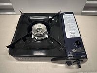 Front angled view of Ranee portable gas stove showing burner, pot supports, and control knob.