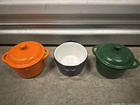 Three mini casserole dishes with two lids visible, positioned on concrete floor.