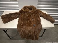 Full view of the brown fur coat laid flat on a table, showing the large decorative buttons and rounded collar.