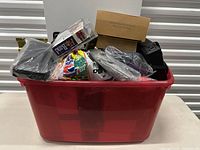Red plastic bin filled with multiple new boxed and bagged household items including the Flip Band game and various cardboard boxes.