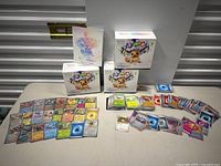 Photo of three unopened Prismatic Evolutions Pokemon booster boxes and a selection of laid out cards including energy and rare Pokemon cards.