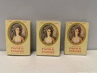 Three vintage packaging boxes of L'Encaresseur Papier Poudré oil blotting paper with identical woman portraits on each box