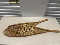 Pair of vintage wooden snowshoes laid flat showing the full length and frame shape.