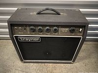 Front view of Traynor TS-25 guitar amplifier showing control panel with knobs and inputs, black speaker grill, and Traynor logo.