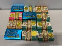 Top-down photo displaying 18 vintage soap bars, including 3 Jade Leaf soaps in blue shiny foil and 15 others with traditional Asian-style paper wrapping and gold seals.