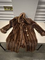 Full view of the vintage women's brown fur coat laid flat on a table.