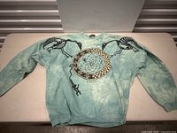 Front view of medium vintage sweater with dreamcatcher and black tribal birds on light blue tie-dye fabric.