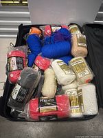Suitcase filled with various Phentex wool yarn skeins in multiple colors and sealed packaging.
