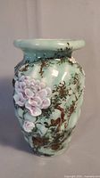 Front view of celadon vase showing applied pink blossoms and painted brown branches over pale green glaze.