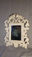 Full front view of antique ornate brass frame painted white with mirror inset reflecting background