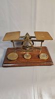 Full view of antique brass balance scale on oak base, showing two weighing pans and central mechanism.