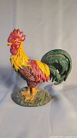 Full side view of the painted cast iron rooster door stop showing red comb, yellow body, and green tail.