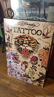 Full view of Ed Hardy tattoo print mounted on panel showing vibrant tattoo flash style artwork featuring tiger, skulls, roses, and swallows.