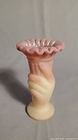 Photo showing full front view of strawberry-cream colored satin glass bud vase with a hand holding the vessel, crimped edge top with iridescent finish.