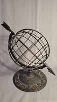 Front view of the cast iron globe compass sundial sculpture showing the spherical cage globe and arrow pointer.