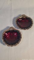 Two scallop shaped dishes with ruby red removable glass inserts placed on white background.