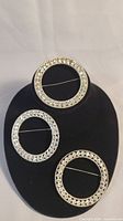 Three matching circular brooches displayed on black stand showing overall shape and size.
