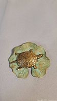 Front view of the brooch showing brass turtle on green patinated lily pad base.