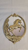 Front view of oval vintage mirror with a brass frame featuring a 3D rearing unicorn and floral designs.