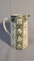 Front view of white semi-porcelain pitcher with green print including 'British Empire' and Canadian emblem under crown.