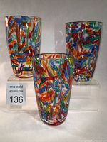 Three hand blown art glass tumblers with colorful confetti patterns displayed together