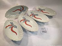 Group photo showing all five scalloped oval plates with red and blue handpainted foliage decoration on a white porcelain base.