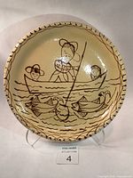 Full view of pottery plate showing three women fishing in a boat with fish in water, decorative rim pattern.