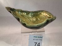 Side angle of the leaf-shaped Raku ceramic dish showing its curved contours and iridescent green glaze.