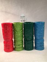All four tiki mugs standing side by side showing front design and colors: red, lime green, verdean green, turquoise