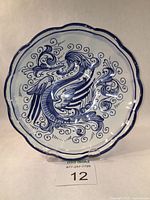 Front view of blue and white Deruta faience plate on stand showing scalloped edges and stylized sea god hand painted in cobalt oxide.