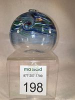 Front view of round blue and copper swirled hand-blown glass oil lamp on clear acrylic stand with lot tag