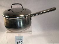 Side view of the stainless steel saucepan with lid on a clear stand showing the full handle and loop lid handle.