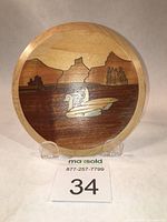 Front view of round wooden plaque featuring marquetry of two geese on water with mountains and trees in the background.